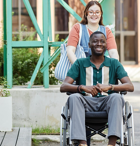 Woman pushing man in a wheelchair outside